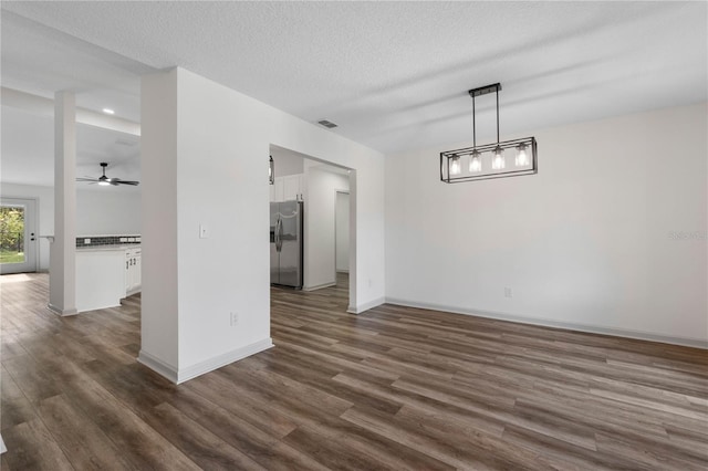 unfurnished dining area with dark wood-type flooring, visible vents, a textured ceiling, and baseboards