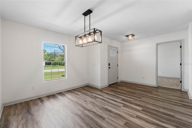 unfurnished dining area with a textured ceiling, baseboards, and wood finished floors