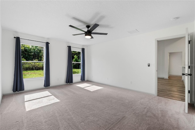 carpeted empty room with ceiling fan, visible vents, and a textured ceiling