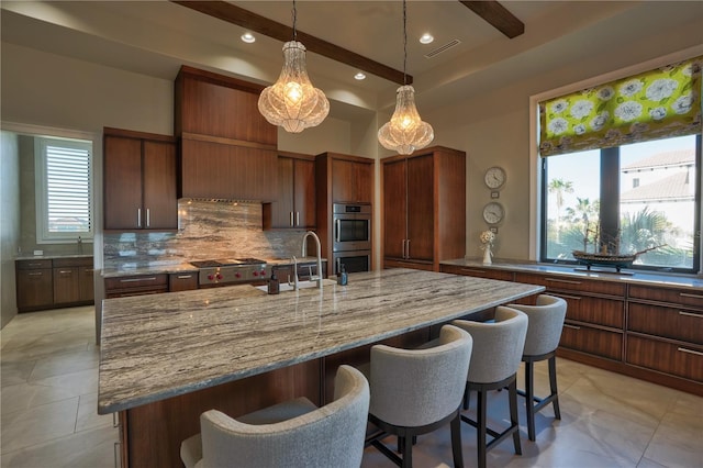 kitchen with decorative backsplash, appliances with stainless steel finishes, a kitchen breakfast bar, sink, and an island with sink