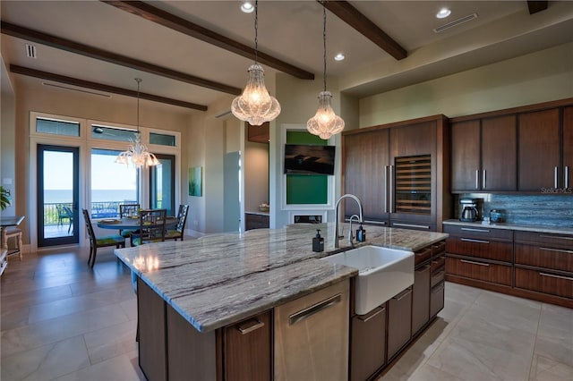 kitchen featuring a center island with sink, sink, beamed ceiling, a notable chandelier, and light stone counters