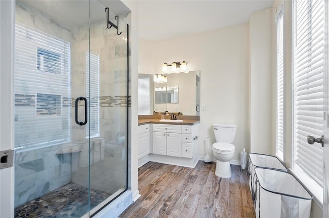 bathroom with hardwood / wood-style floors, vanity, toilet, and a shower with shower door