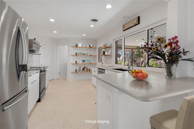 kitchen with kitchen peninsula, white cabinetry, sink, and appliances with stainless steel finishes