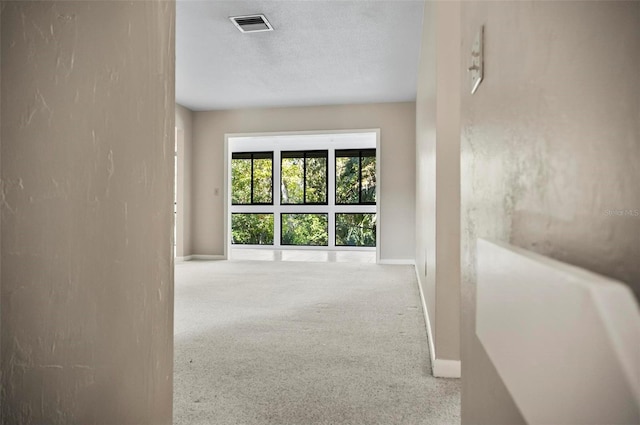 corridor with light colored carpet and a textured ceiling