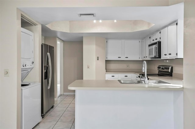 kitchen featuring stacked washer and clothes dryer, white cabinets, light tile patterned floors, kitchen peninsula, and stainless steel appliances