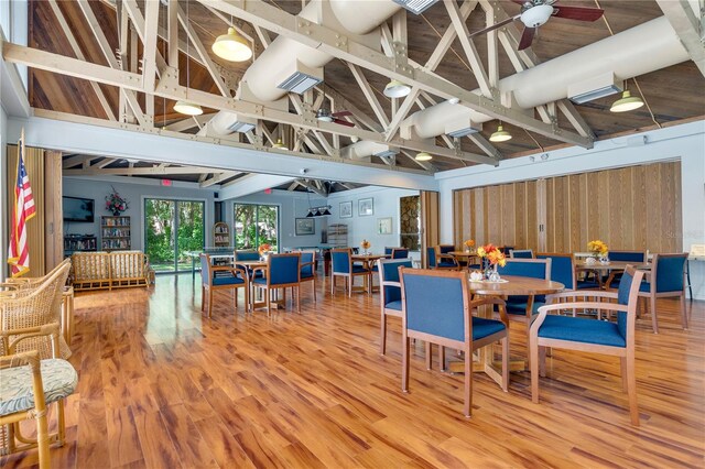 dining space with hardwood / wood-style floors, wood walls, high vaulted ceiling, ceiling fan, and beamed ceiling