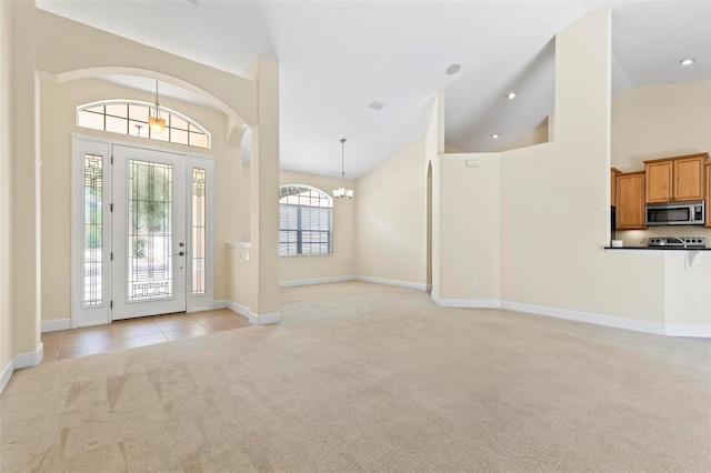 carpeted entrance foyer featuring an inviting chandelier and high vaulted ceiling