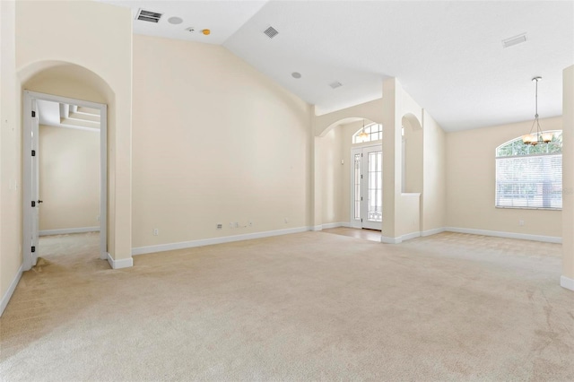 unfurnished living room featuring lofted ceiling, french doors, light colored carpet, and a notable chandelier