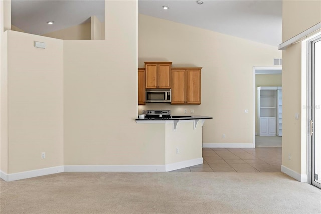 kitchen with high vaulted ceiling, appliances with stainless steel finishes, light colored carpet, and a breakfast bar area