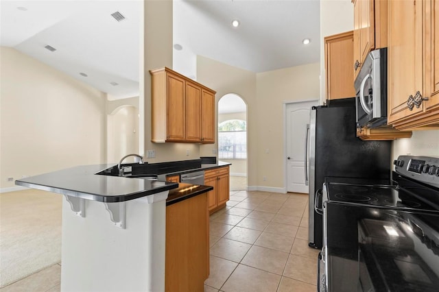 kitchen featuring kitchen peninsula, appliances with stainless steel finishes, a kitchen bar, light tile patterned floors, and vaulted ceiling