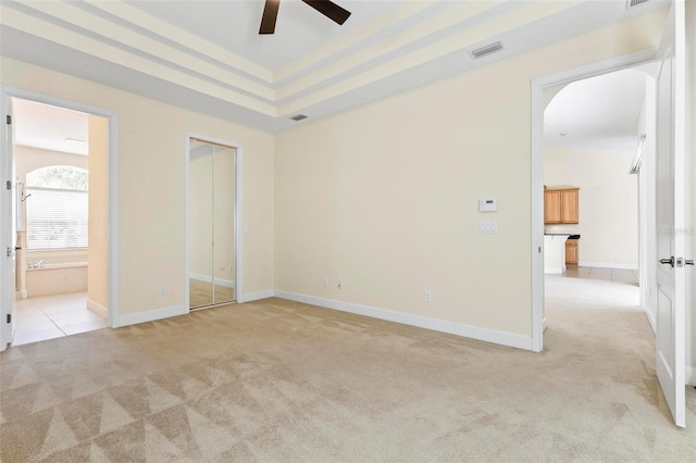 unfurnished bedroom with a closet, light colored carpet, ceiling fan, and connected bathroom