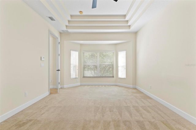 carpeted spare room with ceiling fan and a raised ceiling