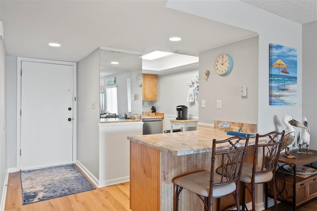 kitchen featuring kitchen peninsula, light brown cabinetry, stainless steel dishwasher, light hardwood / wood-style floors, and a breakfast bar area