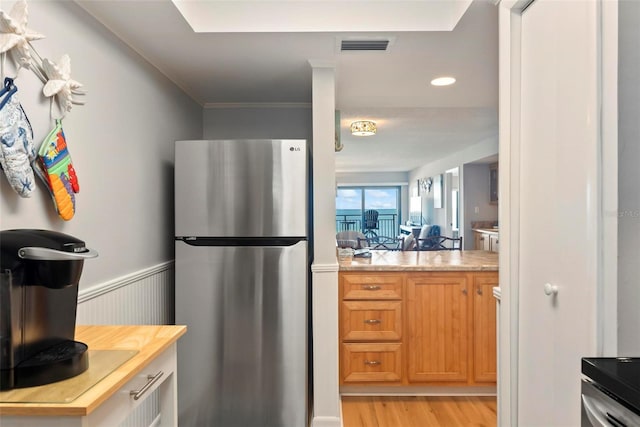 kitchen featuring stainless steel fridge, light wood-type flooring, and ornamental molding