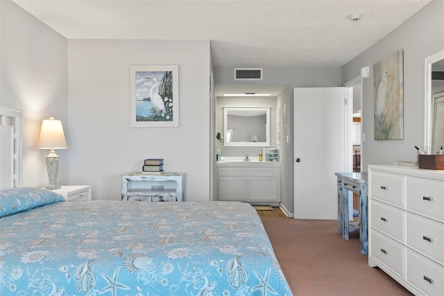 bedroom with ensuite bath, light carpet, sink, and a textured ceiling