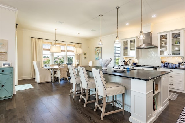 kitchen featuring wall chimney exhaust hood, white cabinetry, a kitchen island with sink, and a wealth of natural light