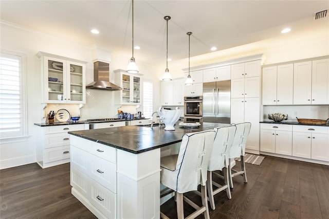 kitchen featuring dark hardwood / wood-style flooring, a center island with sink, stainless steel appliances, and wall chimney exhaust hood