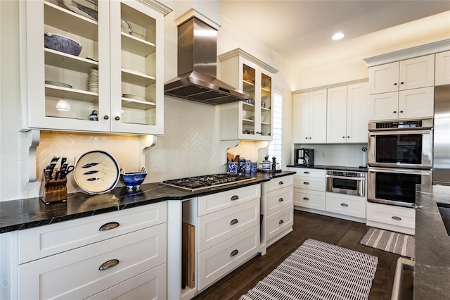 kitchen with dark stone counters, white cabinets, wall chimney exhaust hood, dark hardwood / wood-style flooring, and stainless steel appliances