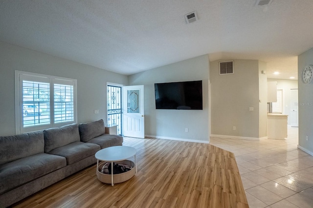 living room featuring a textured ceiling, light hardwood / wood-style flooring, and lofted ceiling