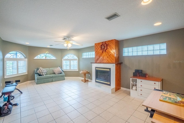 living room featuring ceiling fan, a fireplace, light tile patterned flooring, and a textured ceiling