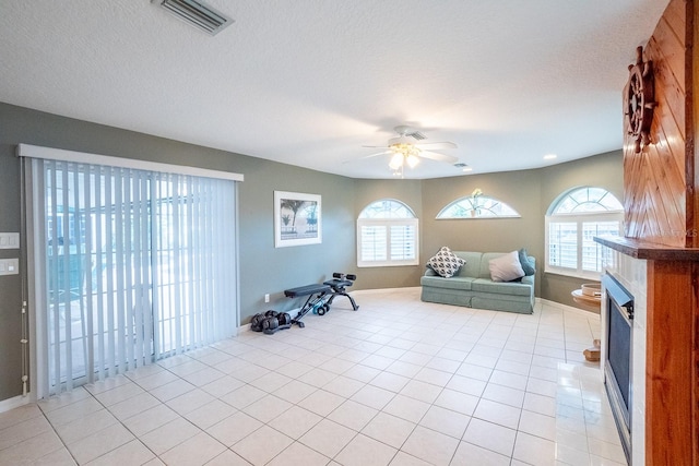 workout room featuring plenty of natural light, ceiling fan, light tile patterned flooring, and a textured ceiling