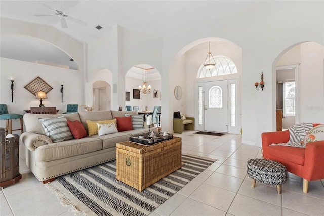 living room with ceiling fan with notable chandelier, light tile patterned flooring, and a high ceiling