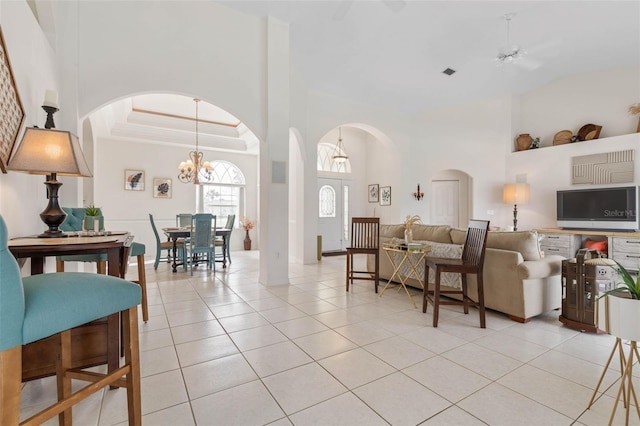 tiled living room featuring ceiling fan with notable chandelier and a towering ceiling