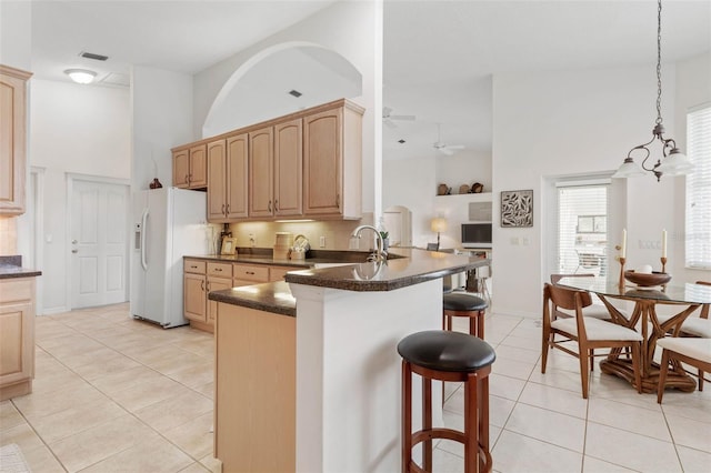 kitchen with kitchen peninsula, white fridge with ice dispenser, high vaulted ceiling, and ceiling fan with notable chandelier