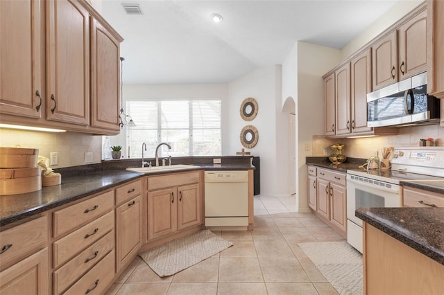 kitchen featuring sink, backsplash, dark stone countertops, white appliances, and light tile patterned floors