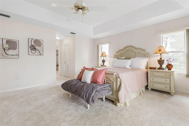 bedroom with a raised ceiling, ceiling fan, and light colored carpet