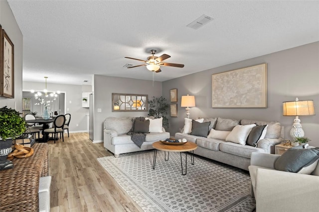 living room with a textured ceiling, ceiling fan with notable chandelier, and light hardwood / wood-style flooring