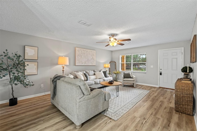 living room with a textured ceiling, ceiling fan, and light hardwood / wood-style flooring