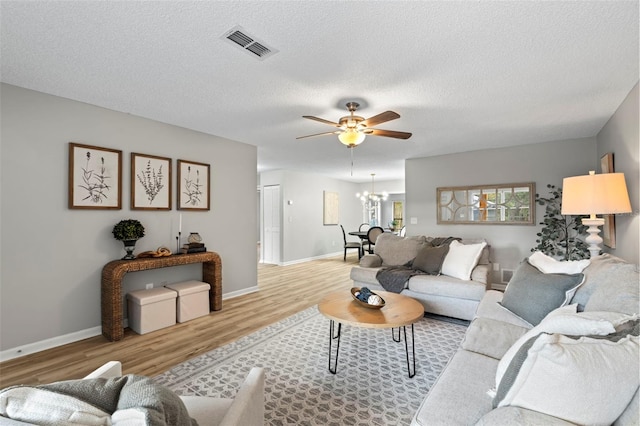 living room featuring a textured ceiling, light hardwood / wood-style floors, and ceiling fan with notable chandelier