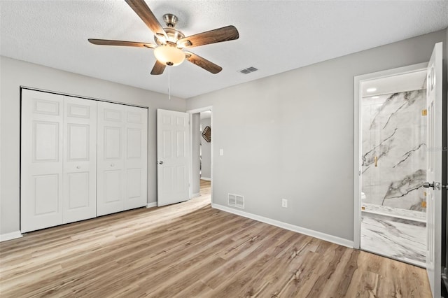 unfurnished bedroom with a textured ceiling, light wood-type flooring, ensuite bath, and ceiling fan