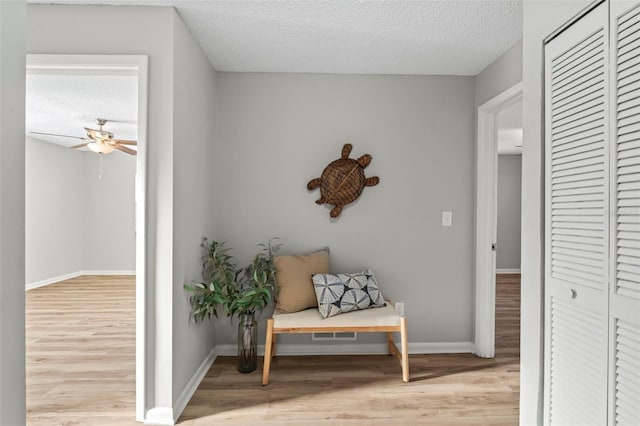 living area with light hardwood / wood-style floors, ceiling fan, and a textured ceiling