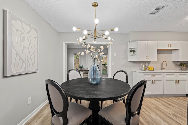 dining room featuring sink, light wood-type flooring, a chandelier, and a textured ceiling