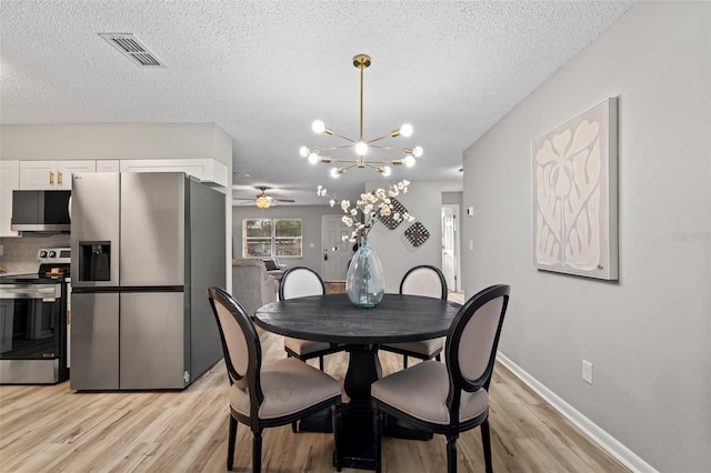 dining area with a textured ceiling, ceiling fan with notable chandelier, and light hardwood / wood-style flooring