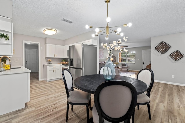 dining space featuring an inviting chandelier, a textured ceiling, sink, and light wood-type flooring