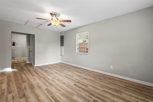 empty room with a textured ceiling, light wood-type flooring, electric panel, and ceiling fan