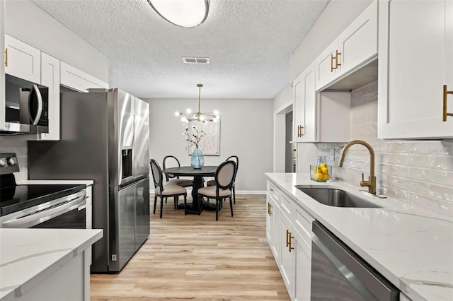 kitchen featuring stainless steel appliances, light wood-type flooring, white cabinetry, hanging light fixtures, and sink