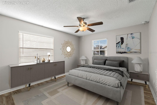 bedroom with a textured ceiling, light wood-type flooring, and ceiling fan