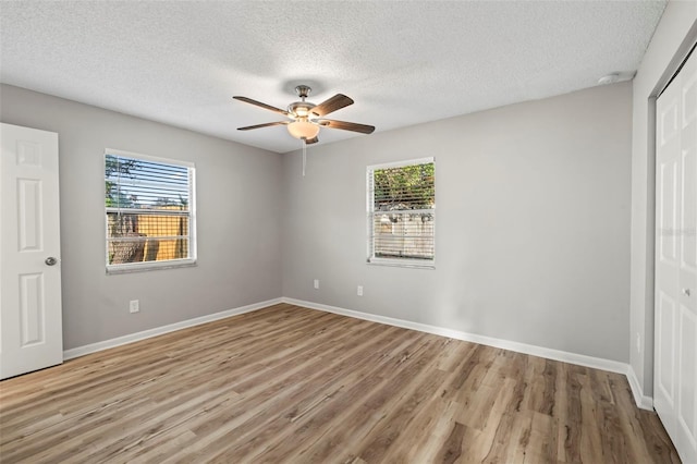 unfurnished bedroom featuring hardwood / wood-style flooring, multiple windows, ceiling fan, and a closet