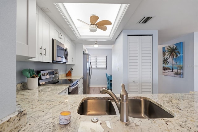 kitchen featuring white cabinets, ornamental molding, a tray ceiling, light stone counters, and stainless steel appliances