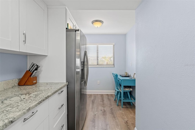 kitchen featuring light stone countertops, white cabinetry, stainless steel refrigerator with ice dispenser, and light hardwood / wood-style flooring