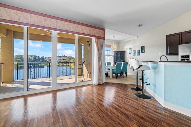 kitchen featuring a breakfast bar, hardwood / wood-style floors, decorative light fixtures, a water view, and dark brown cabinets