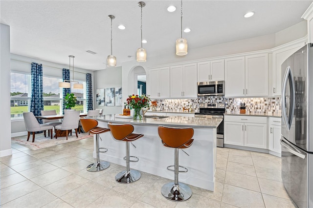 kitchen with white cabinets, decorative light fixtures, stainless steel appliances, and a kitchen island with sink