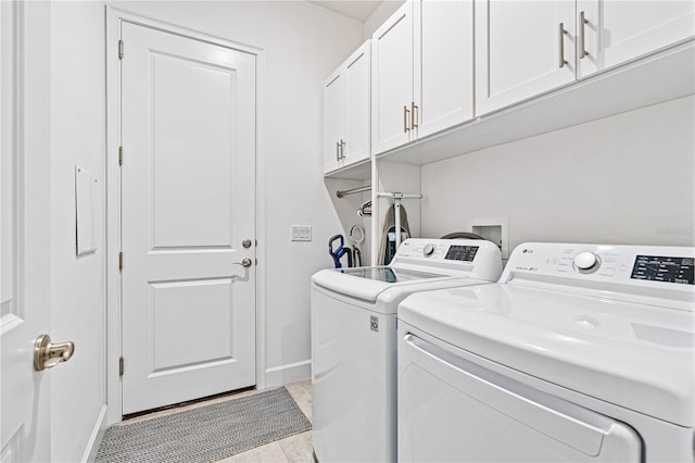 laundry area featuring washing machine and dryer, light tile patterned floors, and cabinets