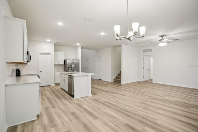 kitchen featuring an island with sink, light hardwood / wood-style floors, pendant lighting, white cabinets, and appliances with stainless steel finishes