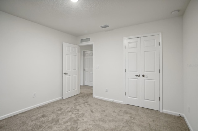 unfurnished bedroom featuring light carpet, a textured ceiling, and a closet