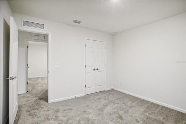 unfurnished bedroom featuring a closet, light carpet, and a textured ceiling